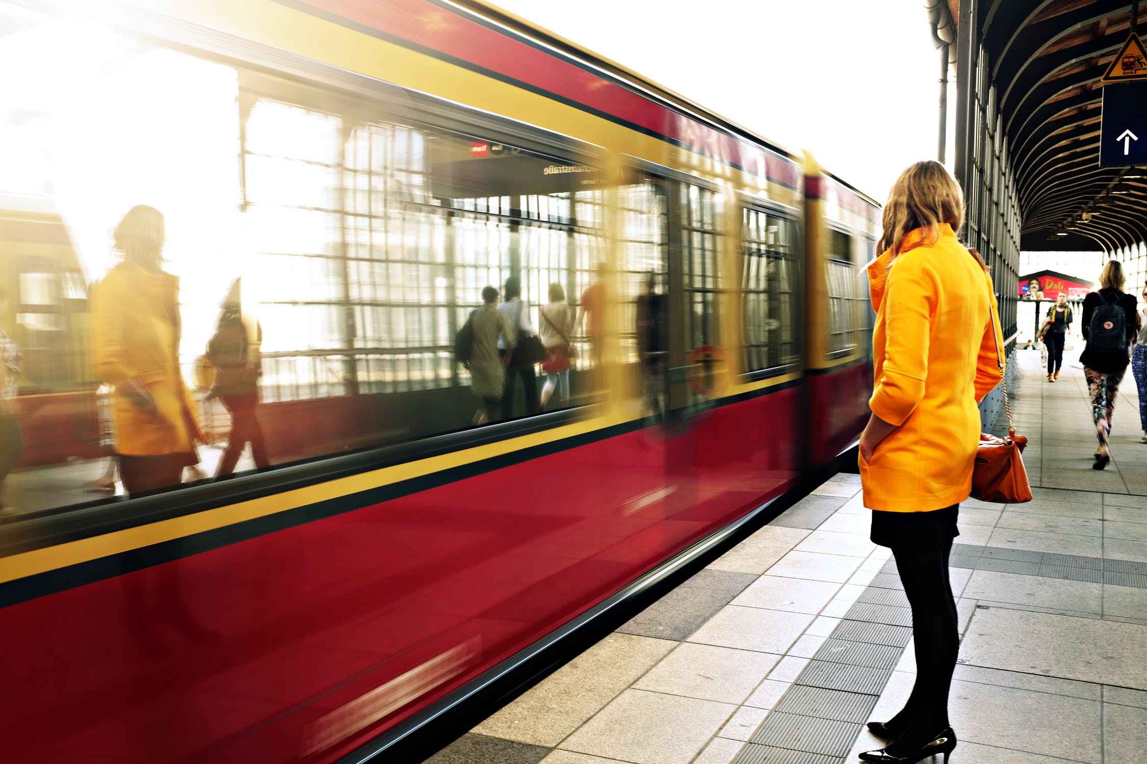 Tram and a woman standing on the platform in a yellow jacket
